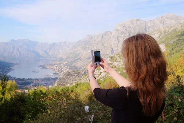 Flicka turist fotograferar ett landskap med havet och bergen i Kotor — Stockfoto