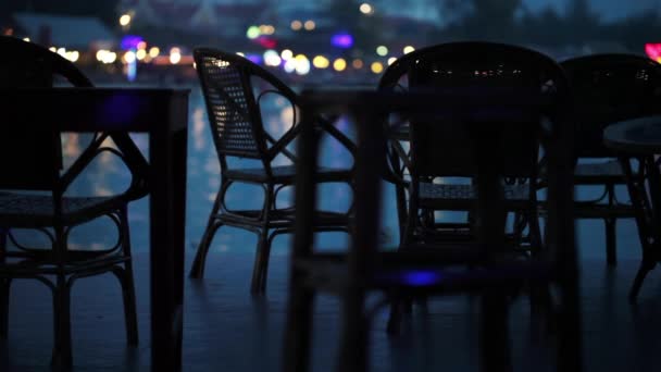 Mesas vacías en el bar en el paseo marítimo con personas que pasan en el fondo — Vídeo de stock