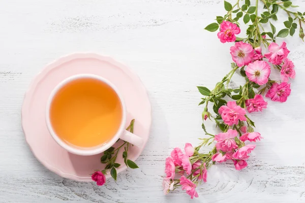 Чашка чаю і гілка троянд на сільському столі . — стокове фото