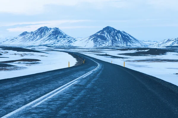 A estrada no crepúsculo através das montanhas cobertas de neve — Fotografia de Stock