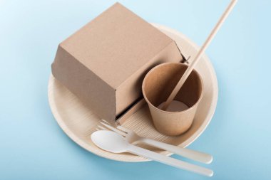 Biyolojik çözünebilir tabak, fincan, hamburger kutusu ve açık mavi arka planda çatal bıçak takımı. Geri dönüşüm kavramı.