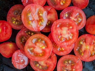 Mevsimlik diyet, beslenme, sağlıklı beslenme. Siyah zemin üzerinde dilimlenmiş kırmızı kiraz domatesleri, su damlalarıyla kaplı domateslerin üst görüntüsü..