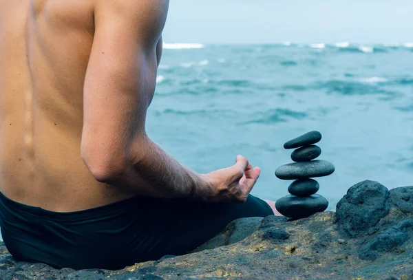 Balancerende stenen gerangschikt in een piramide vorm met een rug van een shirtloze man mediteren — Stockfoto