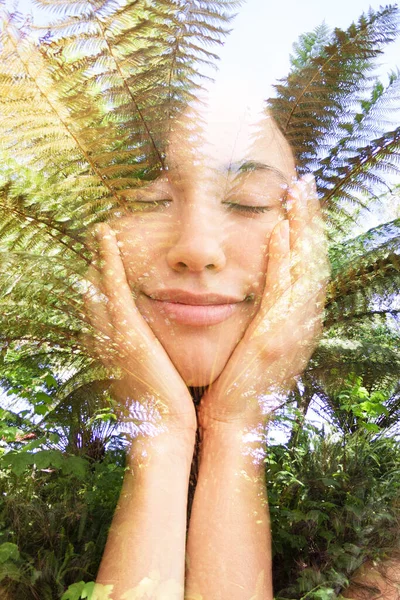 Двойной портрет улыбающейся женщины с закрытыми глазами, держащей подбородок руками и тропической листвой — стоковое фото