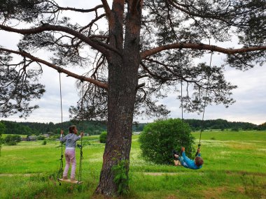 Çocuklar ağaçta salıncakta sallanıyor. Arkadaşlar kırsalda eğleniyor.