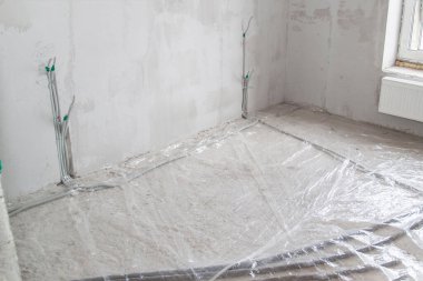 Yeni bir apartman dairesinde elektrik kabloları ve ısıtma boruları döşenmiş radyatör.