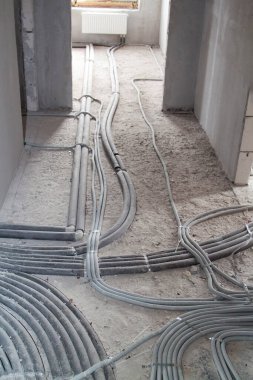 Duvarlar ve zemin boyunca uzanan kıvrımlı elektrik kabloları ve inşaat halindeki bir kır evinde yerden yayılan ısıtma boruları.