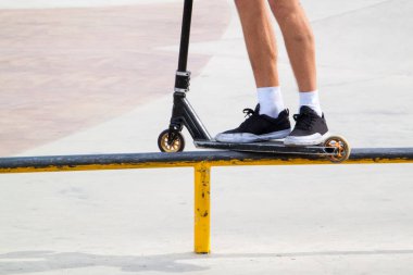 Dublör tekmeli scooter kaykay parkında metal rampanın kenarında kayıyor.