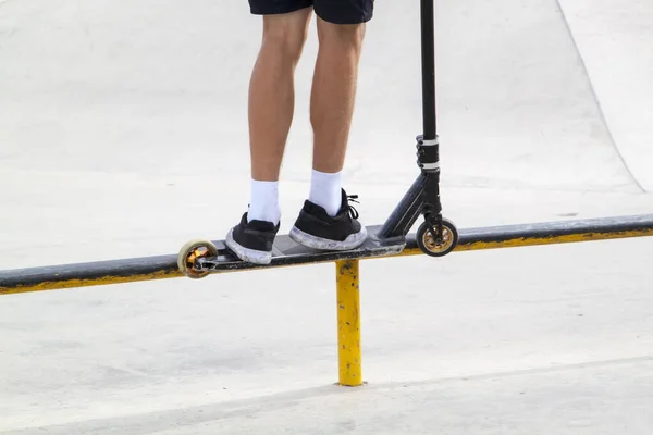 rider on stunt kick scooter slides along edge of metal ramp in skate park