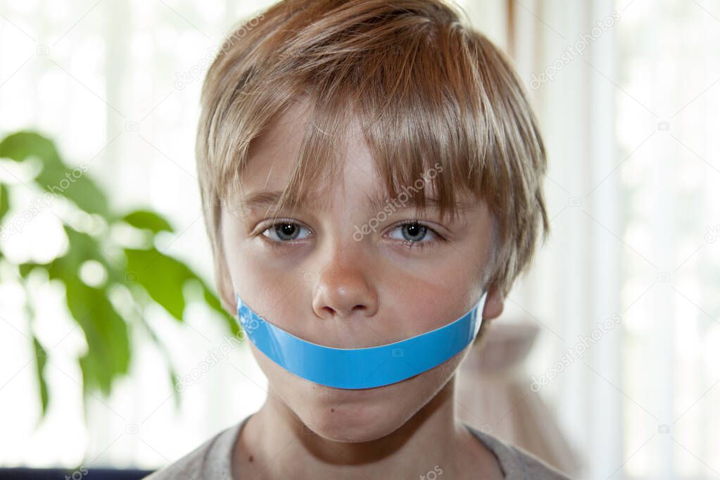 Quiet boy with his mouth taped shut - silenced child concept
