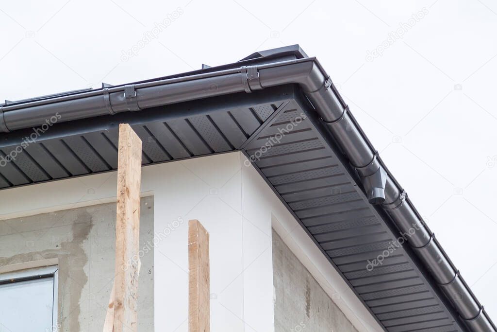 close-up view of corner of house with a gray roof and plums and filing of roof overhangs with soffits of house under construction