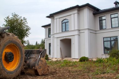 Dozer, doğal bir bölgede yasadışı olarak inşa edilmiş özel bir evi yıkmaya hazırlanıyor. Yakın çekim - kulübenin girişindeki bir traktör kovasının fotoğrafı