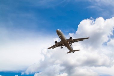 Beyaz yolcu uçağı, beyaz bulutların ve mavi gökyüzünün doğal arka planıyla karaya çıkar.