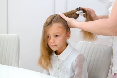 Sakin, üzgün, uzun saçlı liseli kız ve saçını evde tarayan annesi, beyaz bluz giymişler, yaşam tarzı insan konsepti.