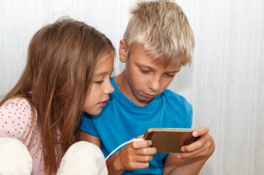 Çocuk yerde oturuyor ve onun telefonunda oyun oynuyor. Kız onun yanına oturur ve bir arkadaşı oynama sürecinden endişe eder.