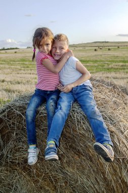 Mutlu çocuk gezginler gün batımında samanlıkta otururlar. Çocuklar, bir kız ve bir oğlan tarlada oturuyor.