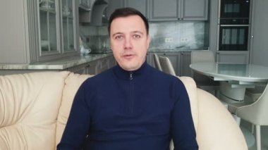 Evdeki kanepede oturan ve kameraya bakan genç bir adam canlı video konferans görüşmesi, video sohbet konsepti yapıyor.