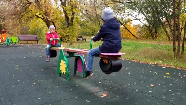 幸せな男の子と女の子は秋の遊び場でスイングに乗る — ストック動画