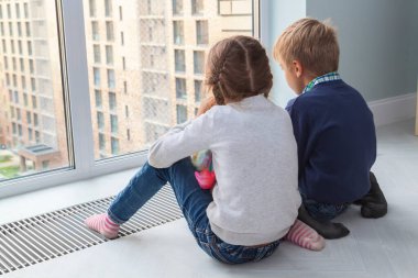 Çocuklar pencere kenarına oturur ve karantina süresince manzaranın tadını çıkarırlar. Saçları örgülü küçük sarışın oğlan ve kız pencereden bir şeye bakıyor.