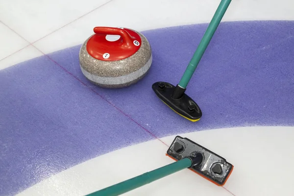 Brooms and stone for curling. view of red curling stone in outer blue ring of house with broom nearby
