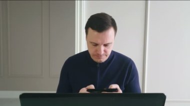 Mutlu insan ev ofisinde çalışmak yerine akıllı telefondan bilgisayar oyunu oynuyor, dizüstü bilgisayarla bir masada oturuyor. Aygıtlara bağlı insanların kavramı.