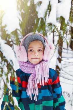 Kar parkında örgü şapka, atkı ve pembe kürk kulaklıklı sevimli küçük kız.