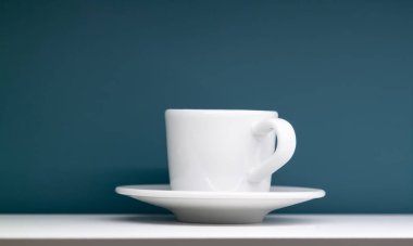 Masada beyaz fincan ve çay tabağı ve arkasında mavi duvar.