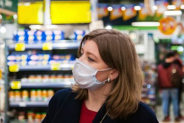 Yeni normal konsept. Coronavirüs krizi ya da kovid19 salgını sırasında raftan alışveriş malzemesi almak isteyen bir kız. Tek kullanımlık tıbbi maske takan genç bir kadın. Salgın hastalık zatürresi