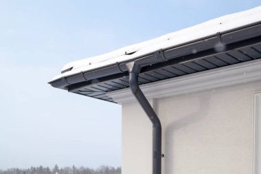 Evin köşesinde yeni gri metal kiremit çatı ve kışın yağmur oluğu var. Metalik Kanalizasyon Sistemi, Boşaltma ve Boşaltma Borusu Dış