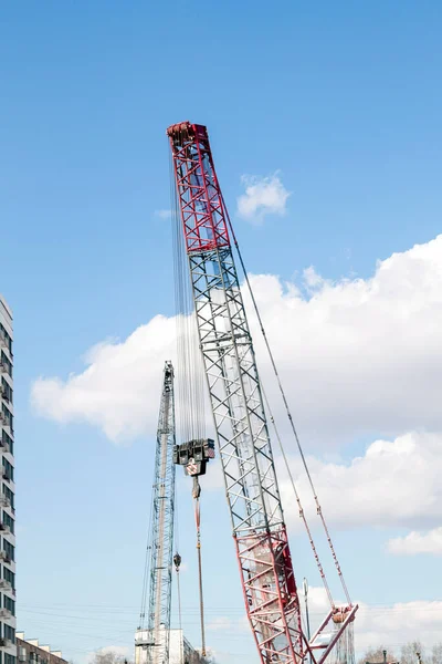 Red lifting crane boom with steel hook against blue sky and white clouds. Red-white crane use reel lift up equipment in construction site. Crane for rent