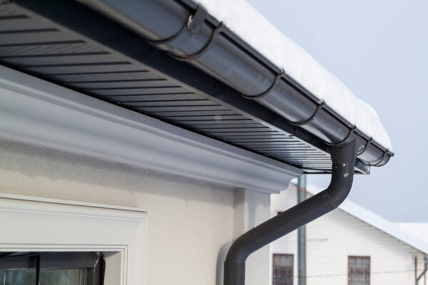 Corner of the house with new gray metal tile roof and rain gutter at winter. Metallic Guttering System, Guttering and Drainage Pipe Exterior