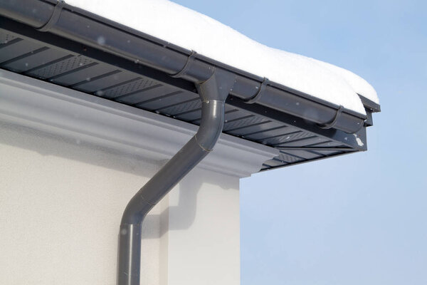 Corner of the house with new gray metal tile roof and rain gutter at winter. Metallic Guttering System, Guttering and Drainage Pipe Exterior