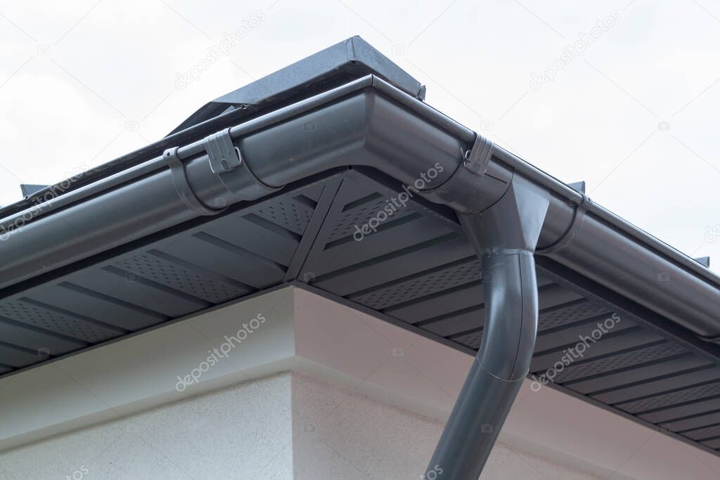 Corner of house with new gray metal tile roof and rain gutter. Metallic Guttering System, Guttering and Drainage Pipe Exterior