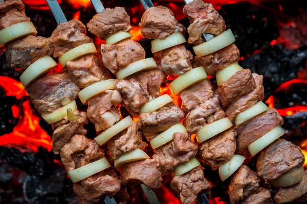 Barbecue spiedini di maiale sulla griglia calda primo piano. Fiamme di fuoco e carboni sullo sfondo — Foto Stock