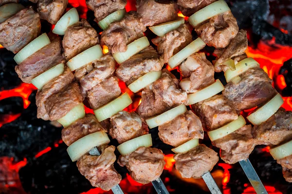Barbecue spiedini di maiale sulla griglia calda primo piano. Fiamme di fuoco e carboni sullo sfondo — Foto Stock