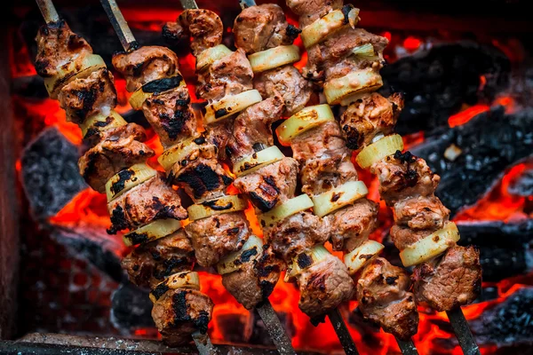 Barbecue spiedini di maiale sulla griglia calda primo piano. Fiamme di fuoco e carboni sullo sfondo — Foto Stock