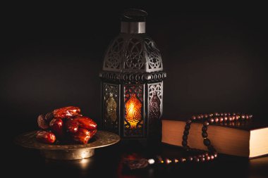Açık bir Müslüman kutsal Kur 'an' ı ile kurutulmuş tarihler. Kutsal Ramazan ayının Müslüman bayramı. Koyu bir arka planda. Parlayan Fanuc feneriyle harika bir arka plan.