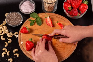 Tahta üzerinde çilek kesen kadın ellerinin yakınlaşması.