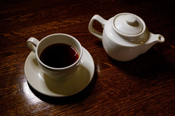 Tea cup and tea pot on table in dark room — Stock Photo, Image
