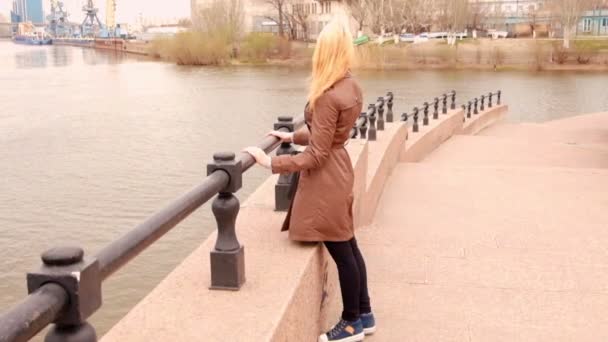 Chica bonita mirando al puerto con grúas mientras se apoya en el terraplén del río en la ciudad . — Vídeos de Stock