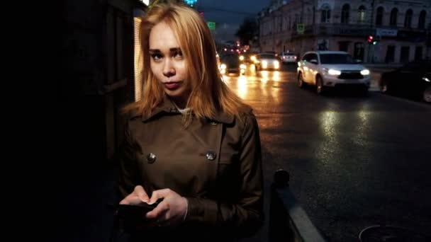 Gelukkige vrouw in de stad in de avond, bewegende auto's op de achtergrond, gestemde schot — Stockvideo