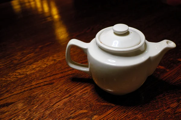 Teapot on old wooden table against the background of dark room — Stock Photo, Image