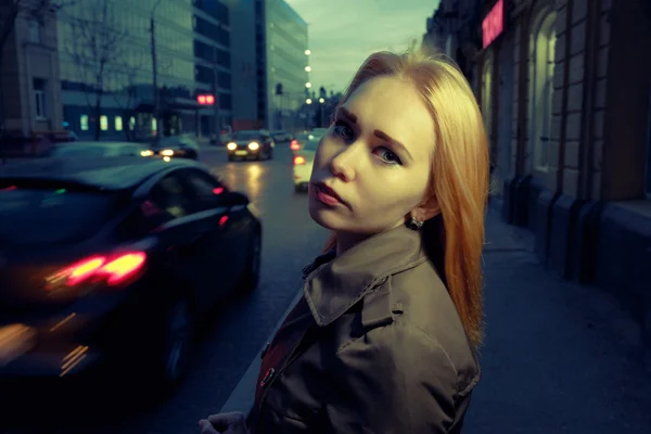 Pretty woman posing in pensive state of mind in the night street with blurred cars and streetlights on background, toned — Stock Photo, Image