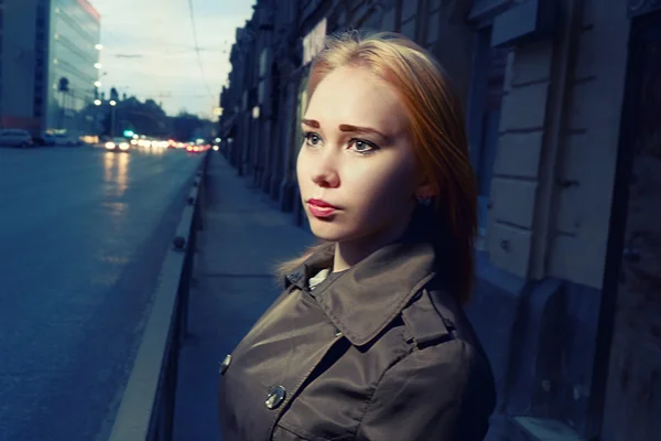 Niedliches Mädchen mit blonden Haaren posiert in der Nacht Straße ob Stadt mit defokussierten Autoscheinwerfern auf dem Hintergrund, getöntes Bild — Stockfoto