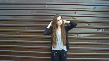 Young long haired brunette posing against brown metal fence, toned image