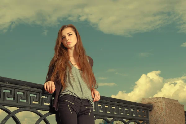 Una chica solitaria espera a que alguien hable. Usando suéter gris claro, pantalones negros, una joven americana parada junto a una cerca de metal, triste, deprimida, perdida en el pensamiento. Copyspace. Efecto Instagram —  Fotos de Stock