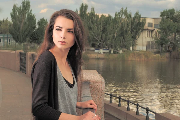 Mooi meisje wacht op je. Het dragen van licht grijs shirt, zwarte jas, een jonge Amerikaanse vrouw permanent door metalen hek op pier in New York, fronste, verdrietig, depressief, ongelukkig, terugkijkend. Instagram effect — Stockfoto