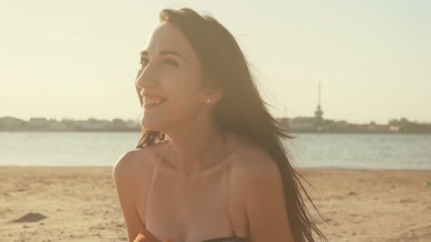 Donna felice seduta su una spiaggia di sabbia in estate retroilluminata dal sole dorato bagliore del tramonto guardando lontano della macchina fotografica godendo di pace, serenità in ambiente naturale, colore vintage — Video Stock