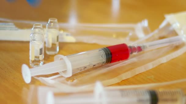 Seringue avec liquide rouge et flacons vides sur le gros plan de la table. Femme en bleu lueur médicale mettre sur la table seringue vide et sortir redy complet pour l'injection de vaccin 