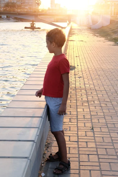Sad boy portrait on embankment backlit, toned image — Stock Photo, Image